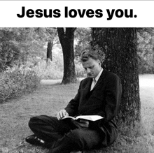 a man in a suit is sitting under a tree reading the bible