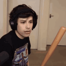 a young man wearing headphones and a black shirt is holding a wooden bat .