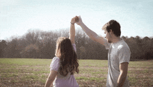 a man and a woman holding hands in a field with trees in the background