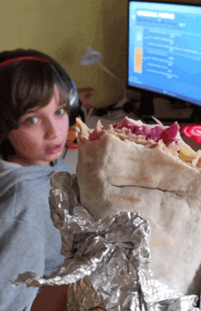 a young boy holding a burrito in front of a computer monitor