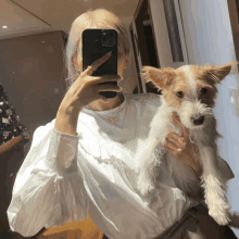 a woman taking a picture of herself with her phone while holding a small dog