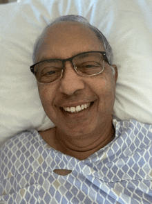 a man in a hospital gown and glasses smiles for the camera