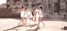 a group of women are dancing in front of a stone wall and the word bin is on the bottom right