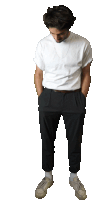 a man in a white t-shirt and black pants stands with his hands in his pockets