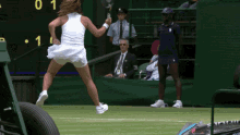 a woman in a white dress is holding a tennis racquet in front of a scoreboard with the number 1 on it