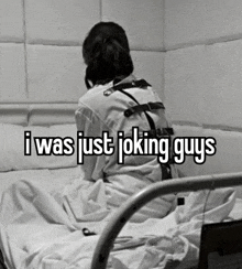 a woman in a straight jacket is sitting on a bed with the words `` i was just joking guys '' .