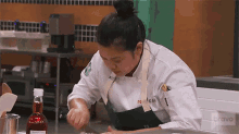 a woman in a chef 's uniform is cooking in a kitchen with bravo written on the wall behind her