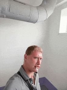 a man smoking a cigarette in a room with pipes on the wall