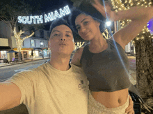 a man and a woman are posing for a selfie in front of a sign that says south miami