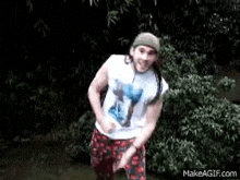 a man wearing a hat and a white shirt is dancing in front of a tree .