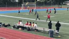 a group of people sitting on a bench watching a soccer game with a player wearing a red jersey with the number 19 on it