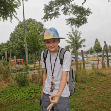 a young boy wearing a hat and a backpack stands in a field