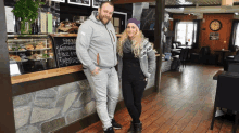 a man and a woman are standing in front of a counter with a chalkboard that says brød