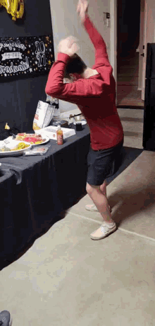 a man in a red shirt is dancing in front of a table with a sign that says ' 20 ' on it