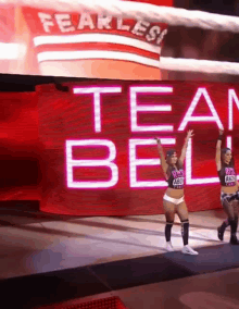 two women are walking in front of a large screen that says fearless team bell