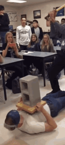 a man is laying on the floor with a brick on his head in front of a group of students