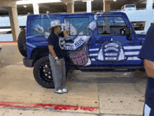 a man in a cowboy hat stands in front of a blue jeep that says tattoo march on the side