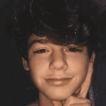 a young boy with curly hair is smiling and holding his hand to his chin .