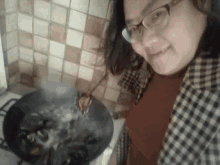 a woman wearing glasses is smiling while cooking on a stove top