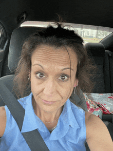 a woman in a blue shirt is sitting in a car with a seat belt around her neck