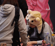 a woman wearing a teddy bear hat sits at a table with a bottle of water in front of her