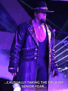 the undertaker is wearing a cowboy hat and a purple coat while standing on a stage .