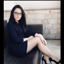 a woman wearing glasses sits on a wicker chair