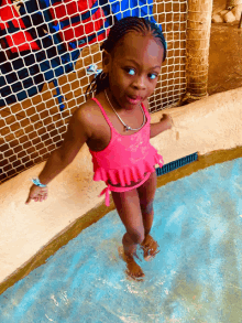 a little girl in a pink bathing suit stands in a pool