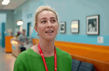 a woman in a green shirt with a red lanyard around her neck is standing in a hospital hallway .