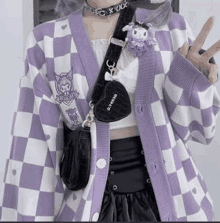 a woman is wearing a purple and white checkered cardigan with a black bag .