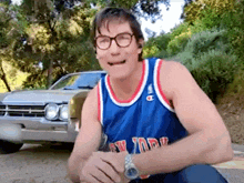 a man wearing a jersey that says new york is sitting in front of a car