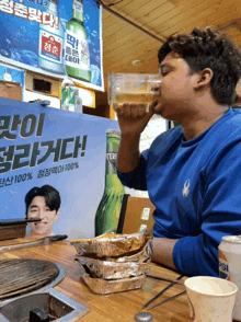 a man drinking from a glass in front of a sign that says 100 % on it