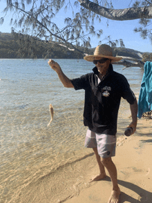 a man standing on a beach holding a fish and wearing a shirt that says ' captain 's ' on it