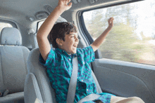 a young boy is sitting in the back seat of a car with his hands in the air .