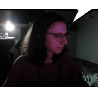 a woman wearing glasses and headphones looks at the camera in a dark room