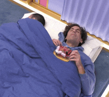 a man laying on a bed with a bowl of strawberries on his chest