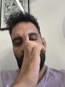 a man with a beard is covering his nose in front of a framed poster that says ' barbers ' on it