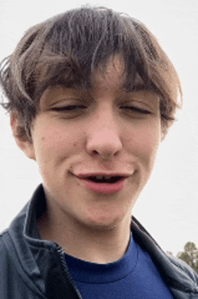 a young man with a blue shirt and a black jacket is smiling with his mouth open .