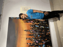 a man wearing a blue shirt that says dream is leaning against a large painting