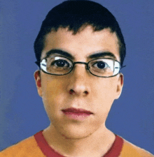 a young man wearing glasses and a red shirt looks at the camera