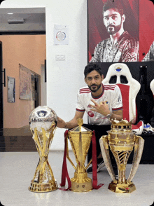 a man posing with three trophies including a soccer trophy