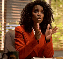 a woman in a red jacket is sitting at a desk and talking