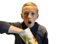 a young boy is holding a bag of popcorn in his hand and making a surprised face .