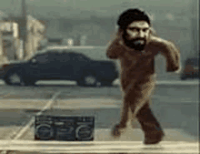 a naked man with a beard is running down a street next to a radio .