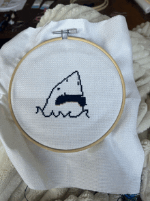 a cross stitch of a shark in a hoop on a table