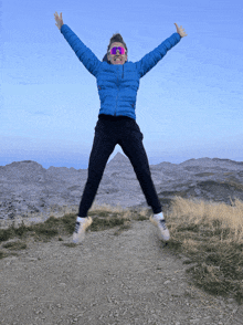 a woman in a blue jacket is jumping in the air with her arms outstretched