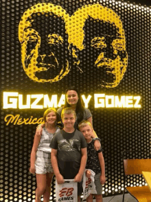 a woman and three children pose in front of a sign that says guzman y gomez mexico