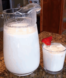 a pitcher of milk and a glass of milk with strawberries on top