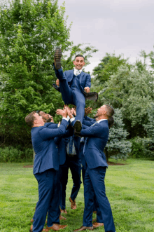 a man in a suit is being lifted in the air by his groomsmen in blue suits