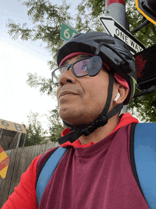 a man wearing a helmet and sunglasses is standing in front of a one way sign